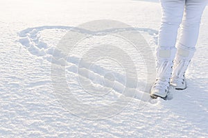 Heart on snow created by footsteps. Woman walks in snow boots. Winter background.