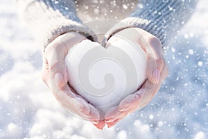 Heart of snow in hands in winter sunny day