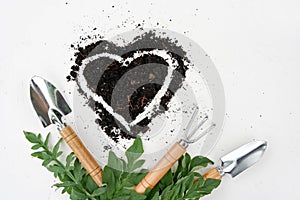 Heart from soil with garden tools and green leaves on white background