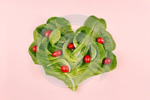 Heart of spring healthy food - cherry tomatoes and leaves spinach on pink background. Valentine`s day backdrop.