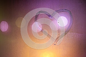 heart symbol hand drawn on wet night window glass in orange colors