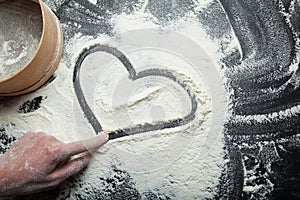 Heart and symbol of love, painted on flour, with a woman`s hand