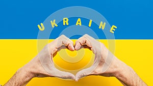 Heart symbol made with hands and Ukrainian flag for background