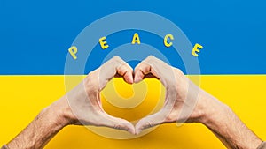 Heart symbol made with hands and Ukrainian flag for background
