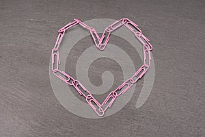 heart symbol made of pink paper clips on a dark background