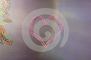 heart symbol made of pink paper clips on a dark background