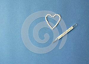 Heart symbol made from white pills and a medical mercury thermometer on a blue background with copy space. Concept for the treatme