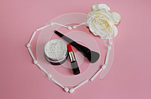 Heart of white shadow applicators on a pink background inside the heart red lipstick
