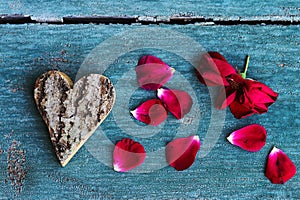 A heart of wood and red rose petals on a green wooden background