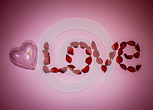 Heart and word love laid out from artificial flowers on a pink background