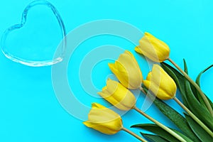 Glass heart and yellow tulips on a turquoise background, fragile love background, valentines day concept