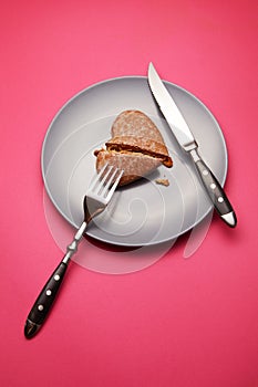 Heartbreaker concept image: heart-shaped cookie on plate with fork and knife over pink background photo