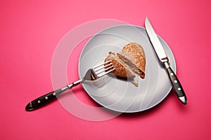 Heartbreaker concept image: heart shaped cookie on plate with fork and knife over pink background photo