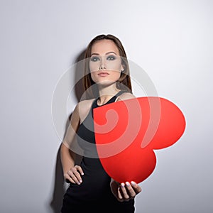 Heartbreaker. Temptress. Seductive woman. Portrait of amazing young fashion woman posing at studio with red heart. Love. Valentine photo