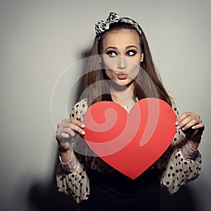 Heartbreaker. Temptress. Seductive woman. Portrait of funny pinup young fashion woman posing at studio with red heart. Love.