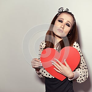 Heartbreaker. Temptress. Seductive woman. Portrait of funny pinup young fashion woman posing at studio with red heart. Love. photo