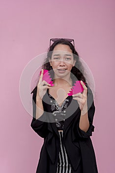A heartbroken young asian woman wails, holding a separated heart shape prop. Isolated on a pink background