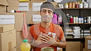 Heartfelt portrait, young, smiling hispanic man, hands on heart, volunteering at charity center, sitting at table in community