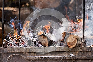 A hearth with burning wood. The logs are engulfed in flames, charred and smoking. Selective focus