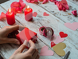 Hearts, gift, ribbons on wooden background. Woman`s hands making handmade valentines day decoration