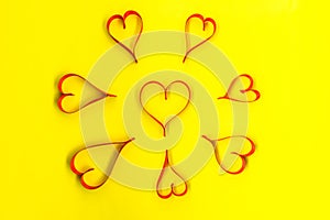 Hearts made from red, satin ribbon on yellow background, view from the top. Valentines Day concept.