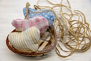 Hearts sewn from scraps in a wicker basket on a light wooden background. A coarse jute thread is twisted nearby