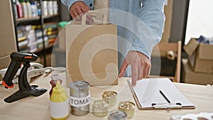 Heartwarming snapshot, handsome young hispanic man packing canned food into paper bag for charity center donation -