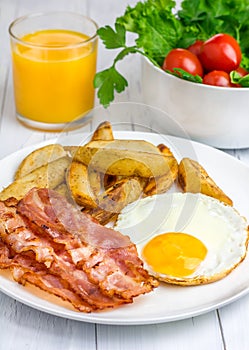 Hearty breakfast with bacon, fried egg, potato and orange juice