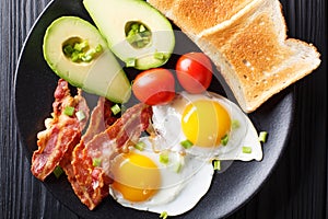 Hearty breakfast: fried eggs with bacon, avocado, toast and toma