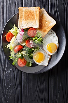 hearty breakfast: fried eggs with fresh vegetable salad and toast close-up. vertical top view