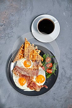 Hearty breakfast of scrambled eggs with bacon, waffles, a salad of greens and tomatoes and a cup of aromatic black coffee