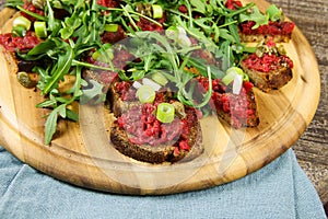 Hearty hefty german snack: isolated wood plate with roasted beef tatar garlic bread, spring onions, capers, pickled cucumbers ghe