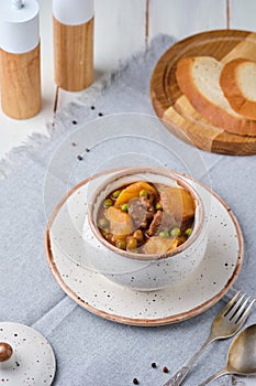 Hearty Irish stew of beef, potatoes and green peas in beer sauce in a ceramic pot on a light wooden background. Irish cuisine