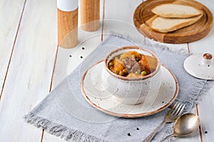 Hearty Irish stew of beef, potatoes and green peas in beer sauce in a ceramic pot on a light wooden background. Irish cuisine