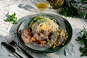 A hearty meal on the table, spaghetti with fried pork chunks, green canned peas and watercress grass. Next to the sauce