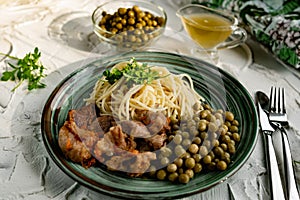 A hearty meal on the table, spaghetti with fried pork chunks, green canned peas and watercress grass. Next to the sauce