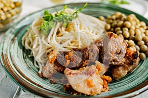 A hearty meal on the table, spaghetti with fried pork chunks, green canned peas and watercress grass. Next to the sauce
