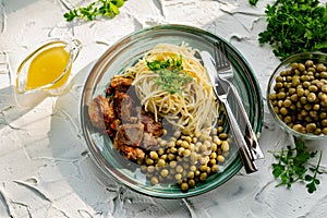 A hearty meal on the table, spaghetti with fried pork chunks, green canned peas and watercress grass. Next to the sauce