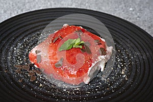 hearty strawberry tiramisu served on a black plate with peppermint, icing sugar