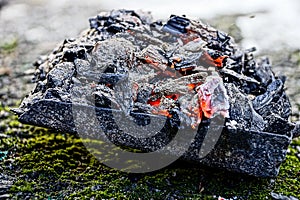 Heat with ash and coals on an iron scoop on a green moss