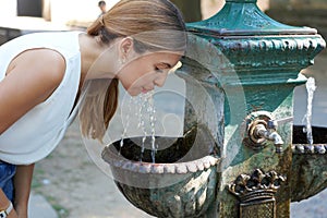 Heat waves concept. Portrait of young woman hydrates herself drinking water from a fountain during a summer hot day photo