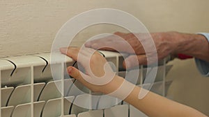 Heating in the apartment concept. The hands of an elderly man and a child check the heat in the house by touching the heating radi