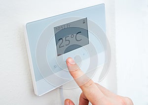 Heating concept. Hand is adjusting temperature in room on digital thermostat control.