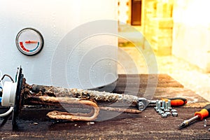 The heating element is covered with rust and scale, with screws on the background of the boiler, lying on a wooden table