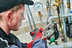 Heating engineer or plumber in boiler room installing or adjusting pipeline