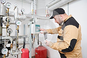 Heating engineer or plumber inspector in boiler room taking readouts or adjusting meter