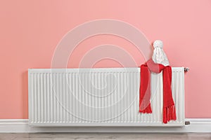 Heating radiator with knitted cap and scarf near color wall.