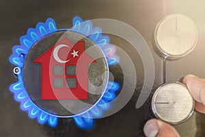 Heating season or gas use in Turkey. Concept, model of a house stands near the flame of a gas boiler on a black photo