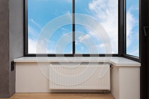 Heating white radiator with adjuster of warming in living room under a large window