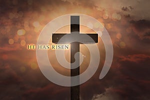 Heavenly scene with Jesus Christ wooden cross elevated on the sky and He has risen text on a sunset background photo